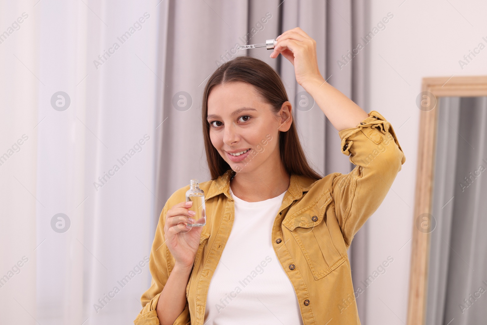 Photo of Beautiful woman applying serum onto hair indoors