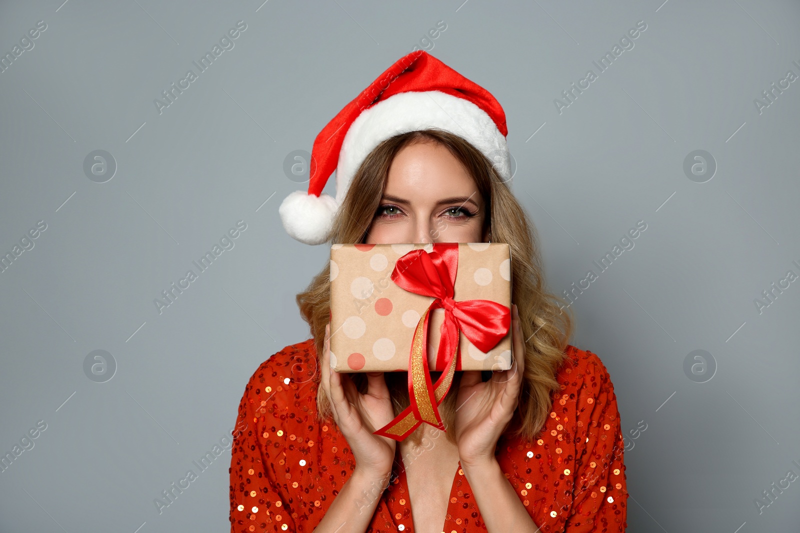 Photo of Happy woman in Santa hat with gift box on grey background. Christmas party