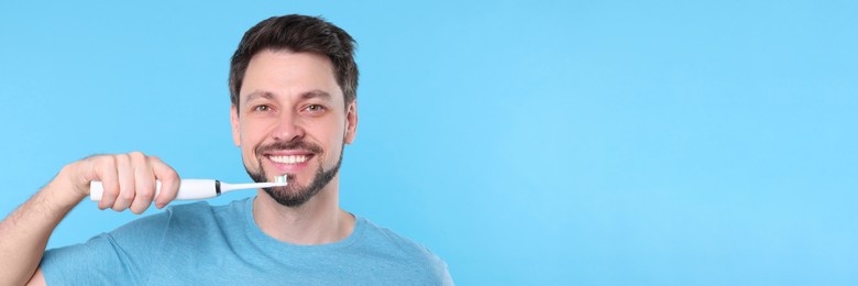 Image of Happy man using electric toothbrush on light blue background. Banner design with space for text