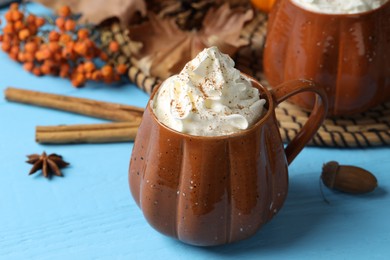 Mugs of pumpkin spice latte with whipped cream on light blue wooden table, closeup