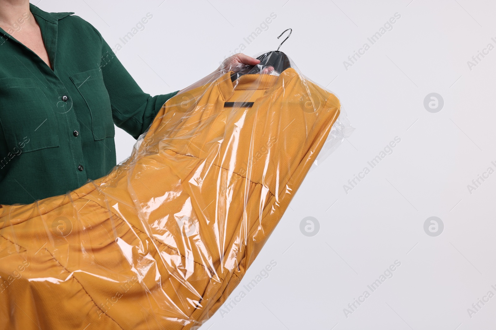 Photo of Dry-cleaning service. Woman holding dress in plastic bag on white background, closeup. Space for text