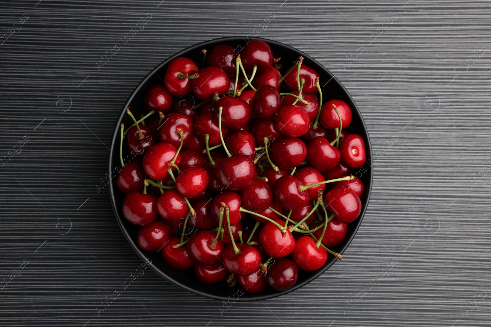 Photo of Bowl with ripe sweet cherries on dark wooden table, top view