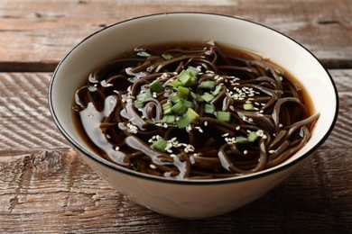 Photo of Tasty soup with buckwheat noodles (soba), onion and sesame in bowl on wooden table, closeup