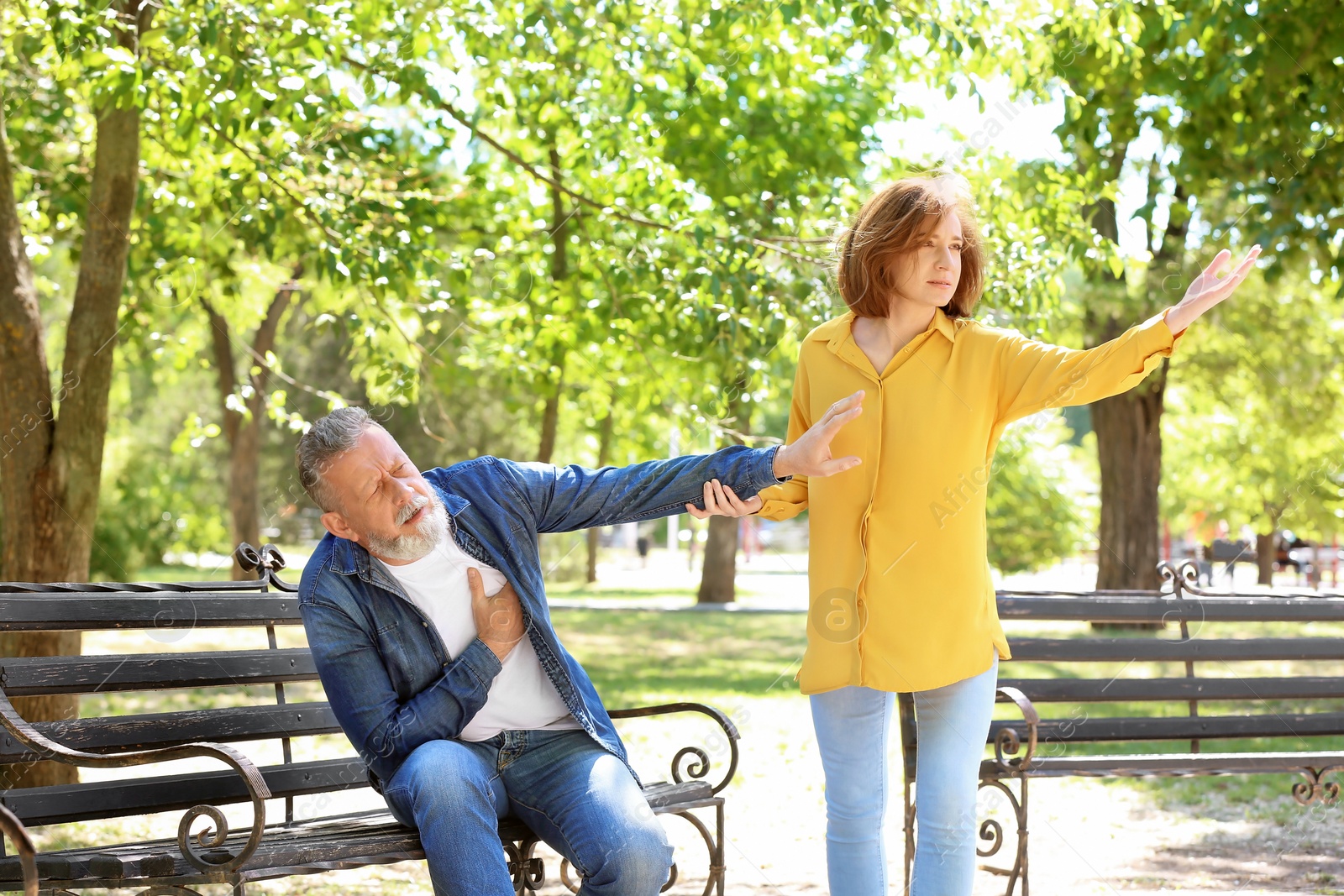 Photo of Woman helping mature man suffering from heart attack on bench in park