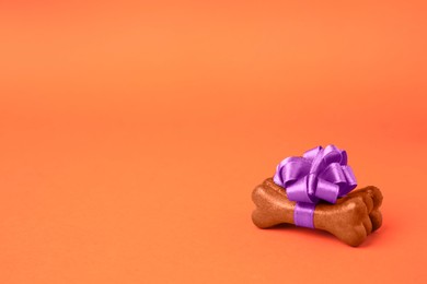 Photo of Bone shaped dog cookies with purple bow on orange background, space for text