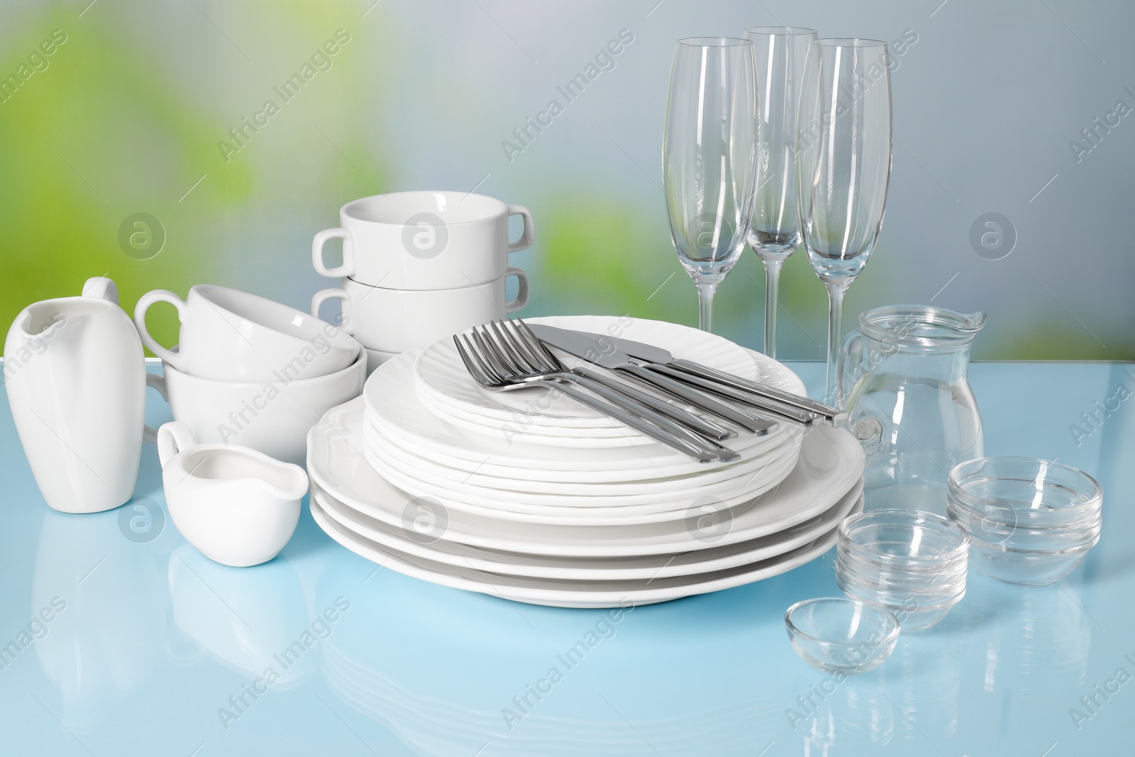 Photo of Set of clean dishes, glasses and cutlery on light blue table