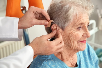 Otolaryngologist putting hearing aid in senior patient's ear at clinic