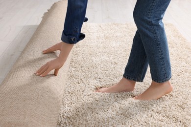 Photo of Woman unrolling carpet on floor in room, closeup