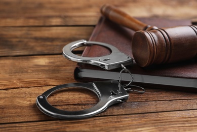 Photo of Gavel, handcuffs and book on wooden table, closeup. Criminal law