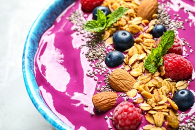 Delicious acai smoothie with granola and berries in dessert bowl on table, closeup