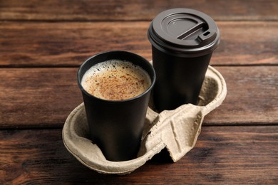 Photo of Takeaway paper cups with coffee in cardboard holder on wooden table