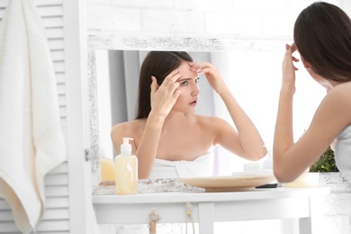 Photo of Teenage girl with acne problem looking in mirror indoors