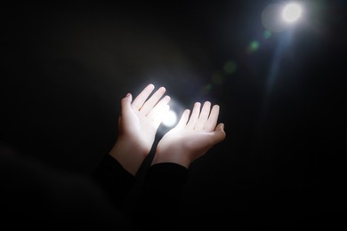 Image of Woman stretching hands towards light in darkness, closeup. Praying concept