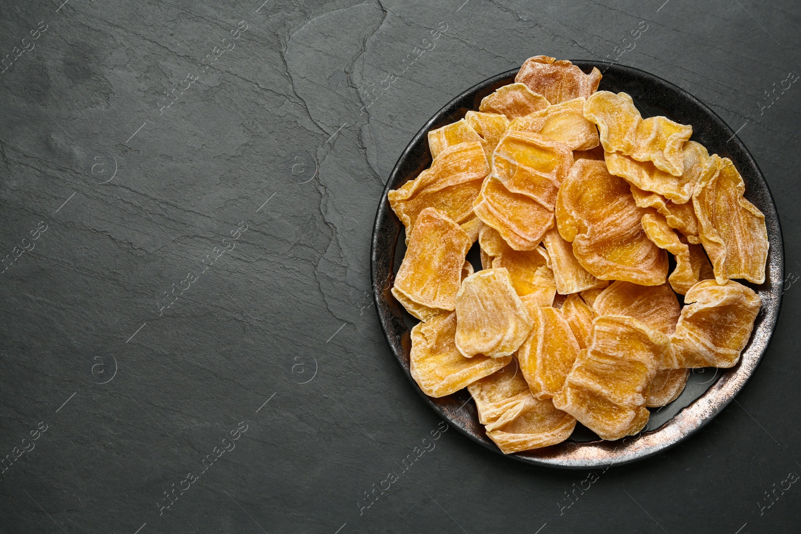 Photo of Delicious dried jackfruit slices on black table, top view. Space for text