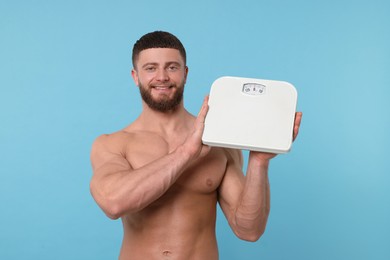 Photo of Happy athletic man holding scales on light blue background. Weight loss concept