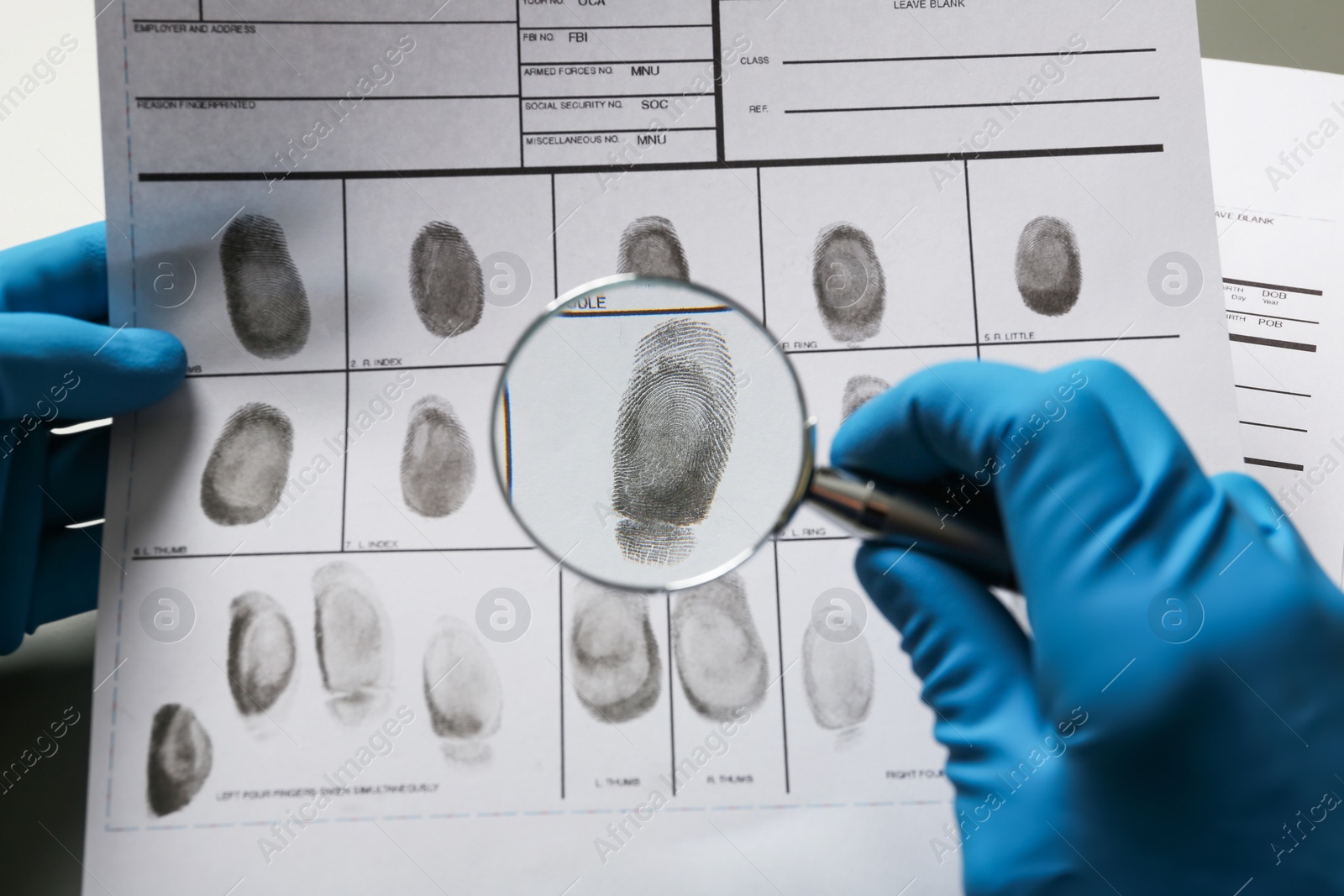 Photo of Criminalist exploring fingerprints with magnifying glass, closeup