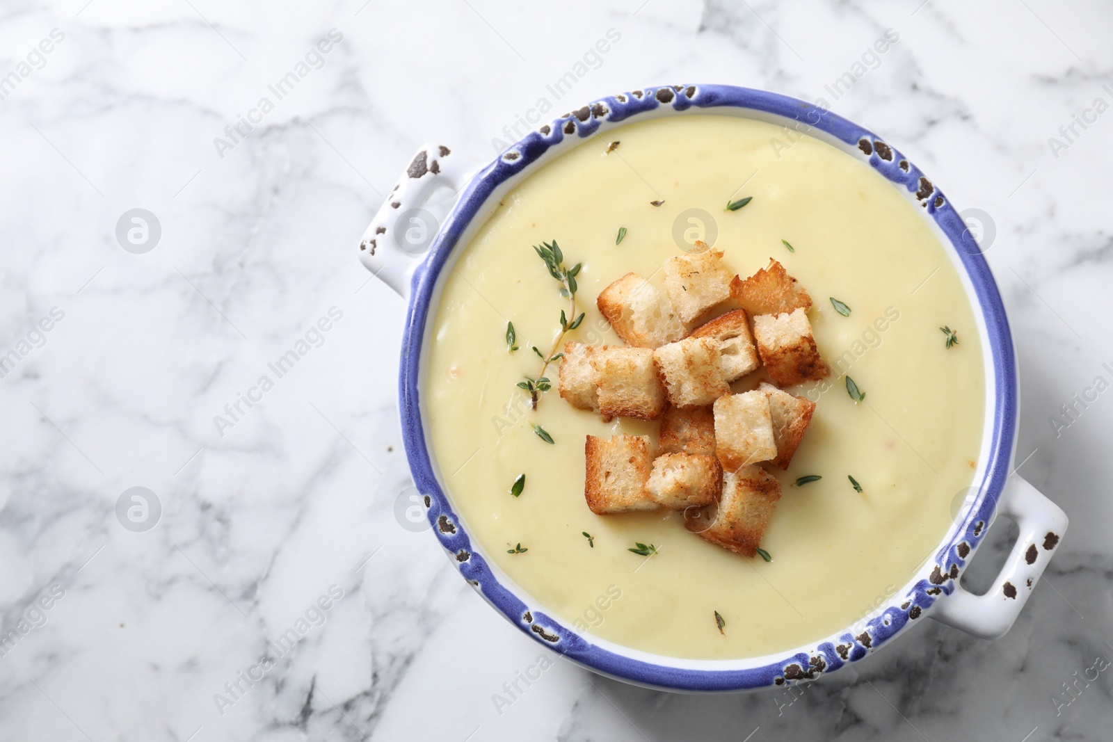 Photo of Tasty potato soup with croutons and rosemary in ceramic pot on white marble table, top view. Space for text