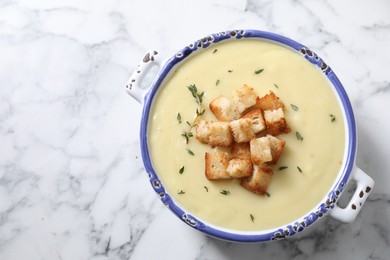 Tasty potato soup with croutons and rosemary in ceramic pot on white marble table, top view. Space for text