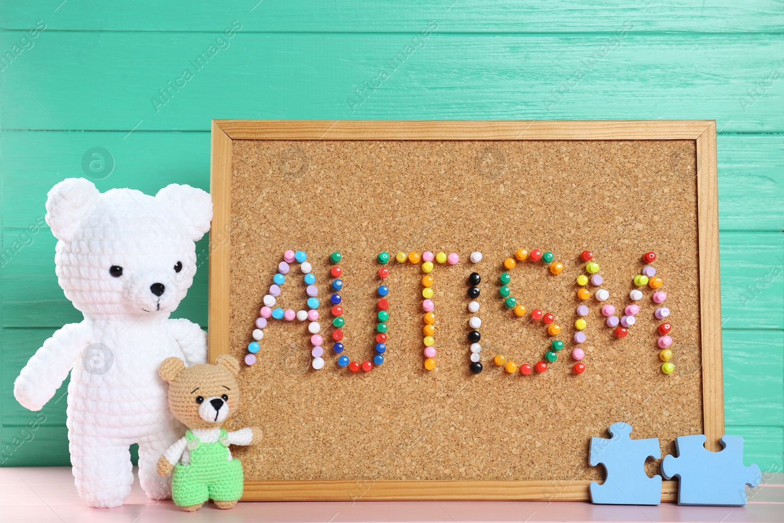 Photo of Cork board with word Autism made of colorful pins and toys on pink wooden table