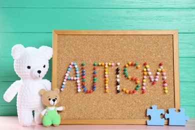 Photo of Cork board with word Autism made of colorful pins and toys on pink wooden table