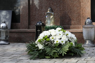 Funeral wreath of flowers and lanterns near grave outdoors