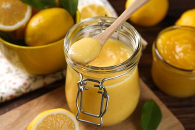 Delicious lemon curd in glass jars, spoon and fresh citrus fruits on table, closeup