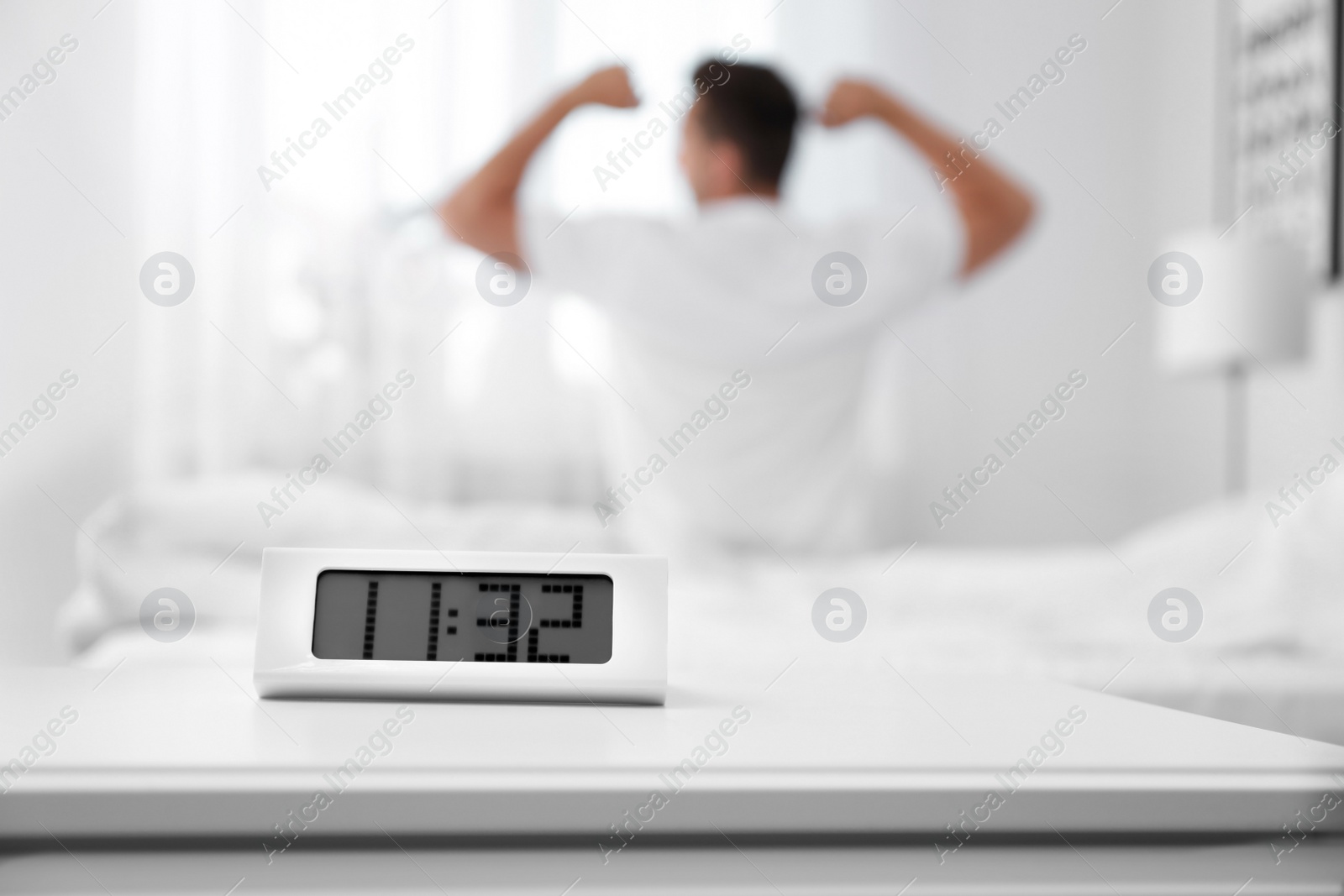 Photo of Digital alarm clock and blurred man on background. Time of day