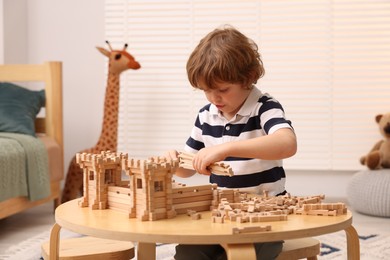 Little boy playing with wooden entry gate at table in room. Child's toy