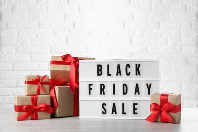 Photo of Lightbox with words Black Friday Sale and gift boxes on wooden table against white brick wall