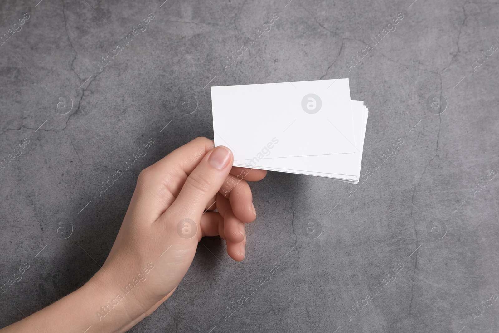 Photo of Woman holding blank cards at grey table, top view. Mockup for design