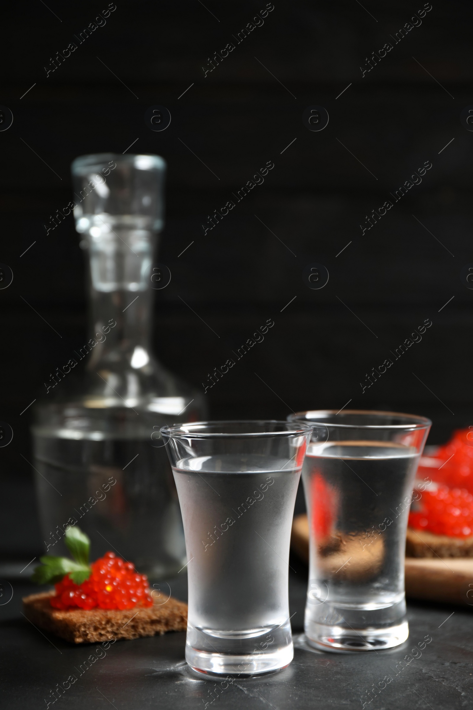 Photo of Cold Russian vodka and sandwiches with red caviar on black table, closeup