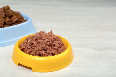 Different pet food in feeding bowls on white table. Space for text