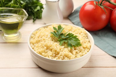 Delicious bulgur with parsley in bowl, tomatoes and oil on wooden table, closeup