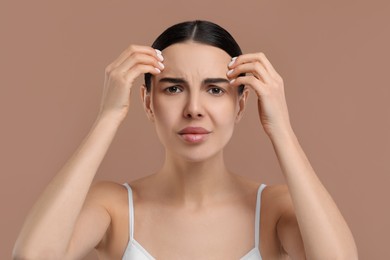 Photo of Woman with dry skin checking her face on beige background