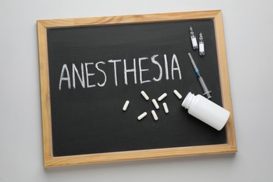 Photo of Blackboard with word Anesthesia, syringe and drugs on light grey background, top view
