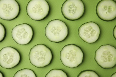 Photo of Fresh slices of cucumbers on green background, top view