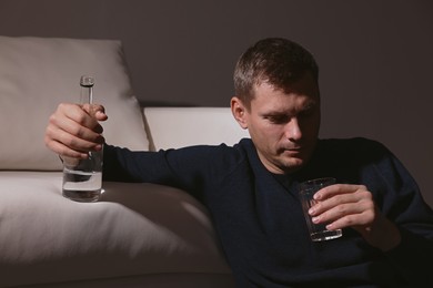 Addicted man with alcoholic drink near sofa indoors