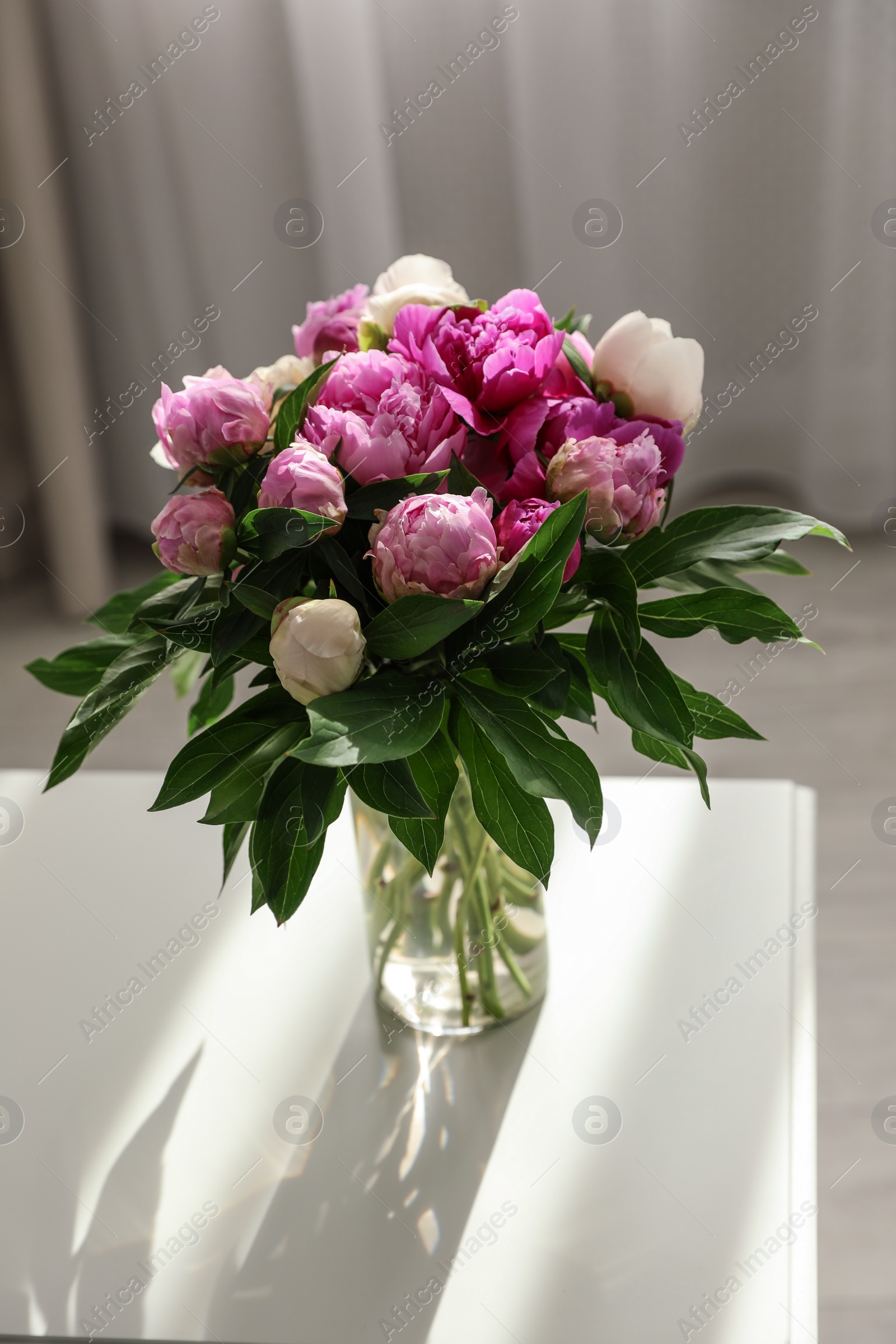 Photo of Vase with bouquet of beautiful peonies on table in room