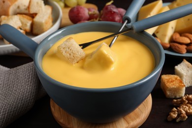 Pot of tasty cheese fondue and forks with bread pieces on wooden table, closeup