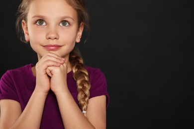 Girl with clasped hands praying on black background, space for text