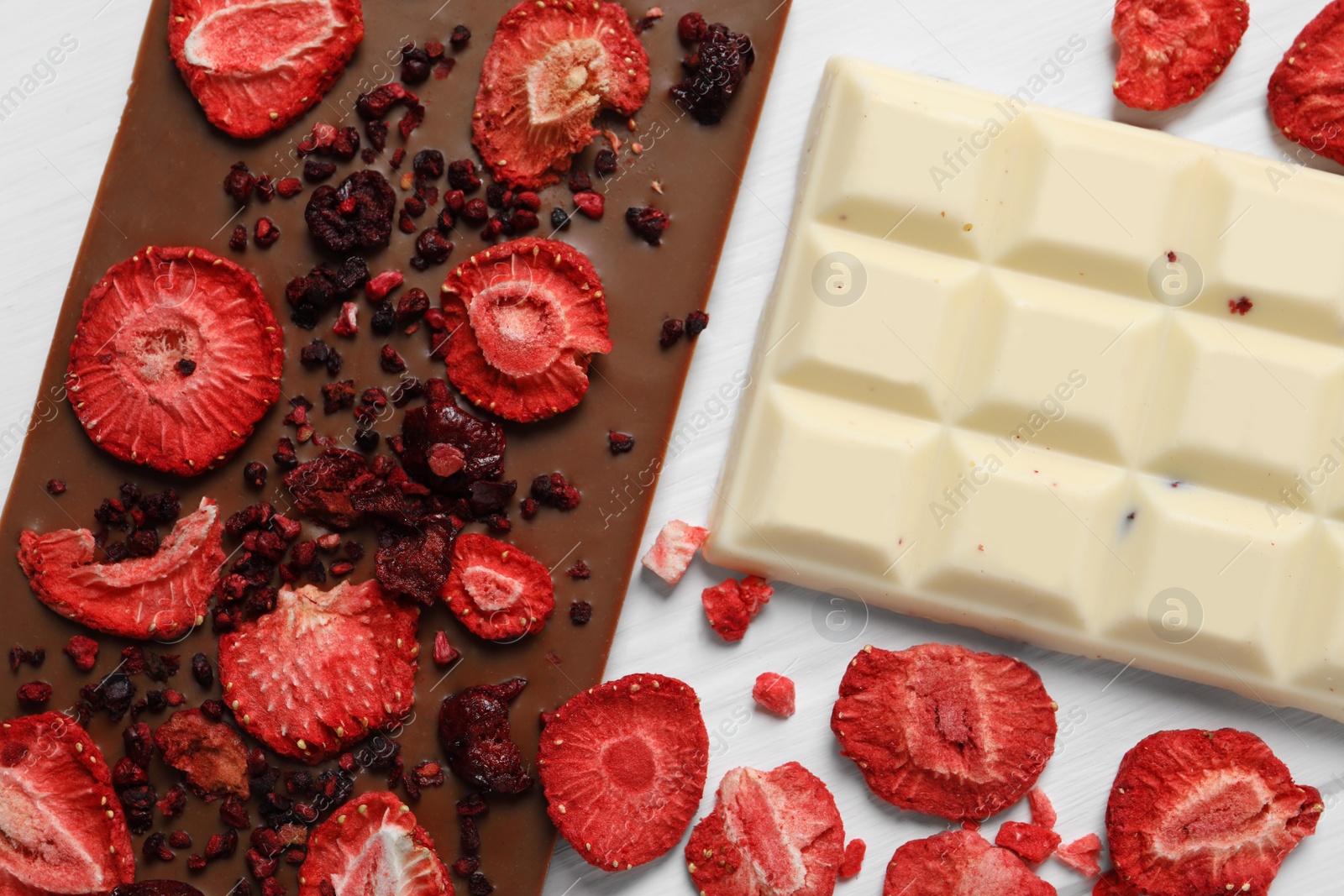 Photo of Different chocolate bars with freeze dried fruits on white wooden table, flat lay