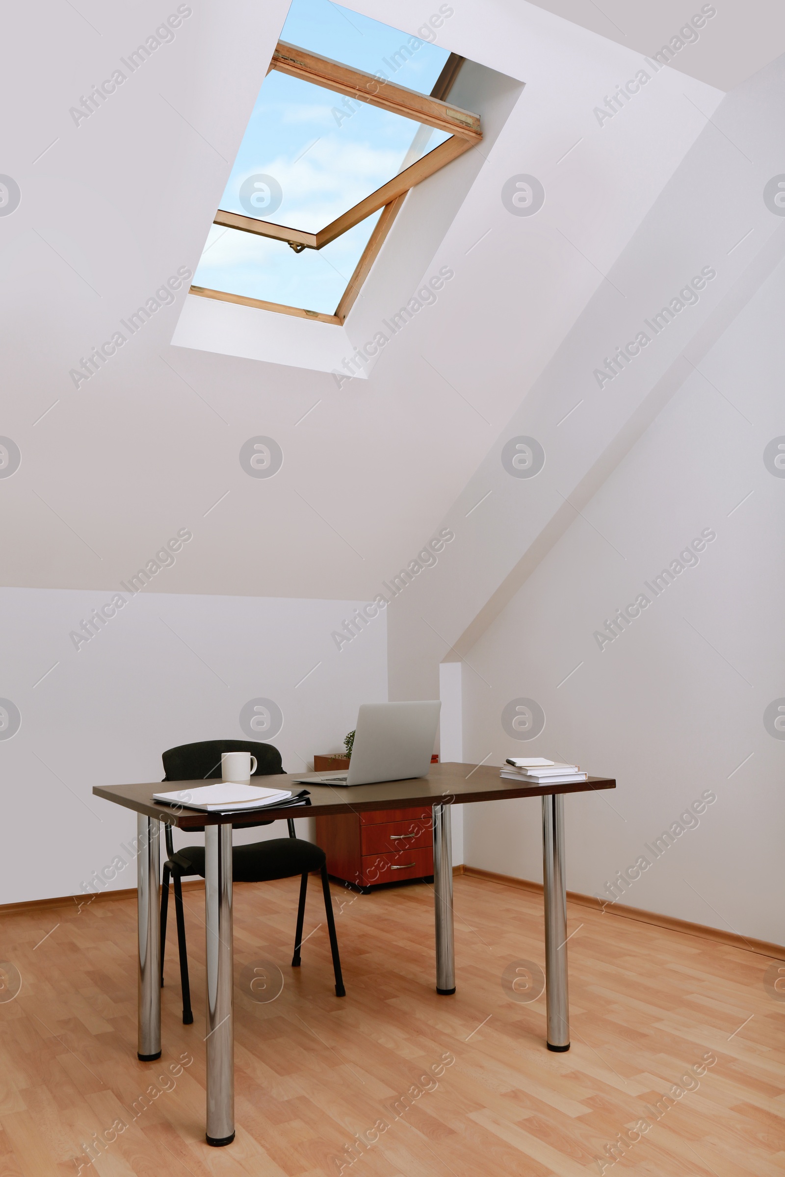 Photo of Stylish workplace with laptop and documents in attic room. Interior design