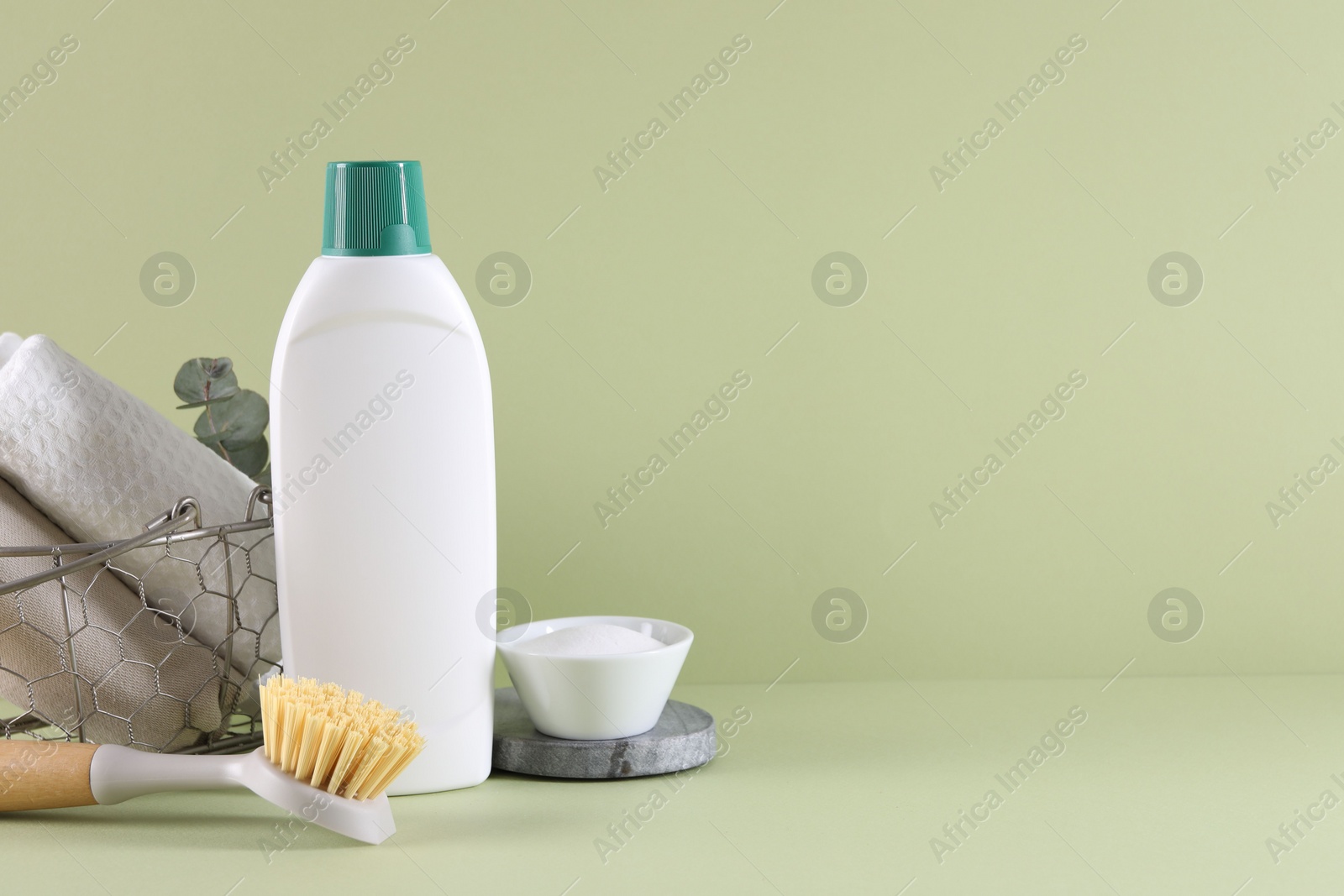 Photo of Bottle of cleaning product, rags, baking soda and brush on light green background. Space for text