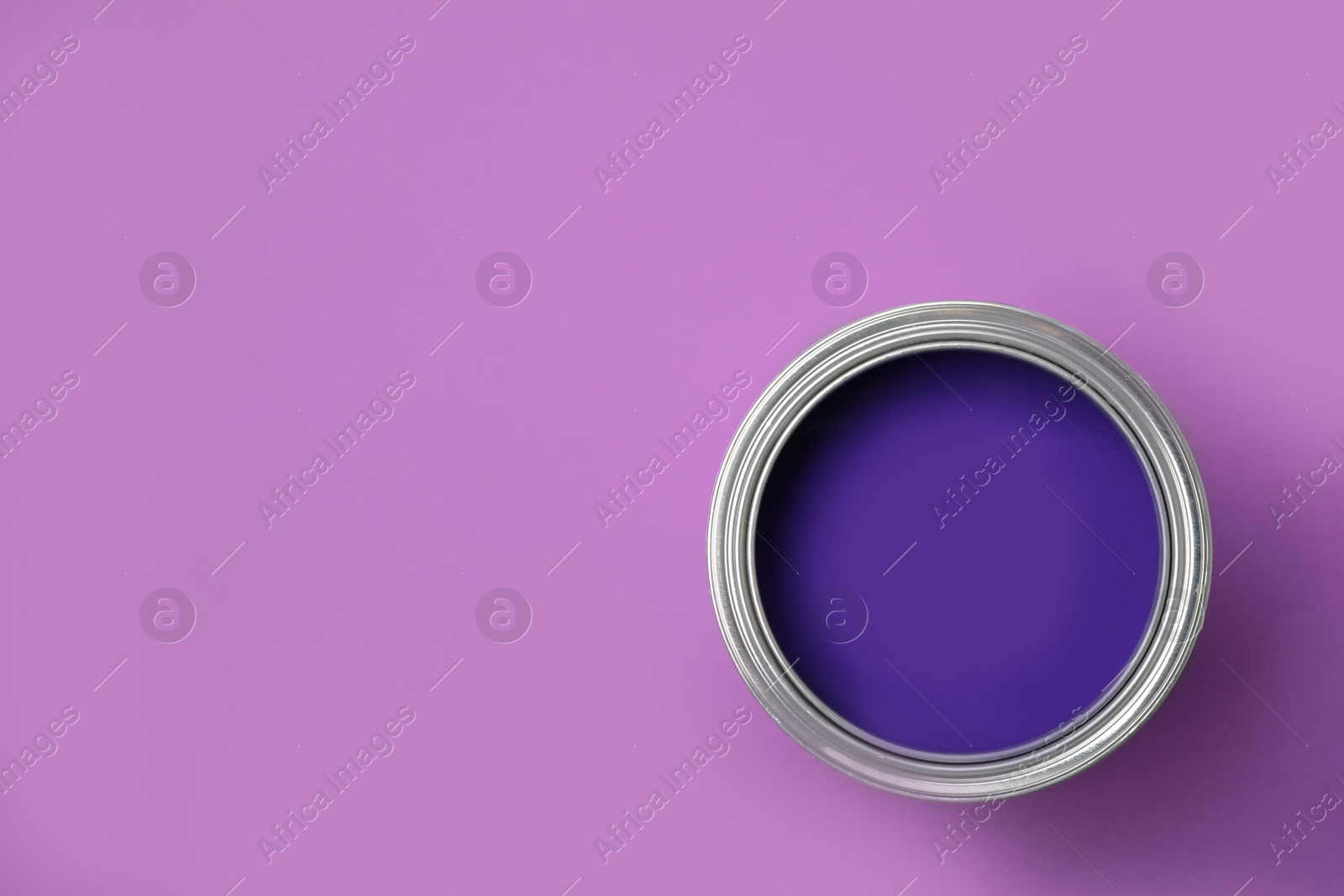 Photo of Open can of paint on violet background, top view. Space for text