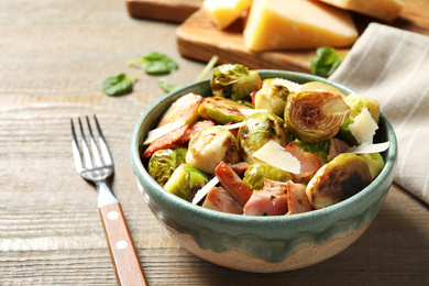 Image of Delicious fried Brussels sprouts with bacon in bowl on wooden table