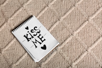 Photo of Notebook with phrase Kiss Me and hearts on knitted fabric, top view. Space for text