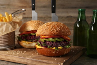 Photo of Tasty vegetarian burgers served with french fries and beer on wooden table