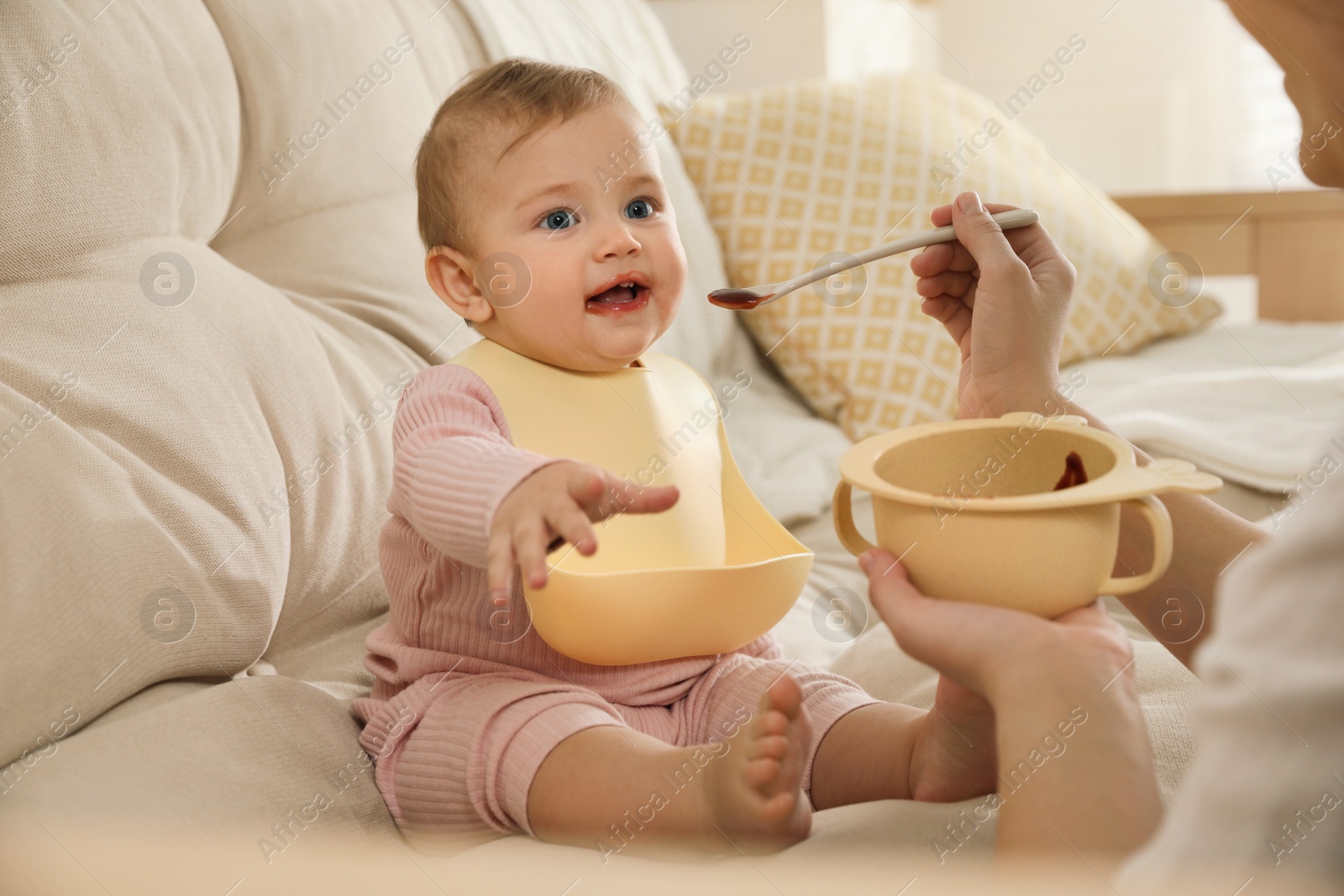 Photo of Mother feeding her little baby at home. Kid wearing silicone bib