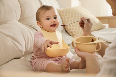 Photo of Mother feeding her little baby at home. Kid wearing silicone bib