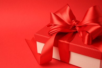 Beautiful gift box with bow on red background, closeup. Space for text
